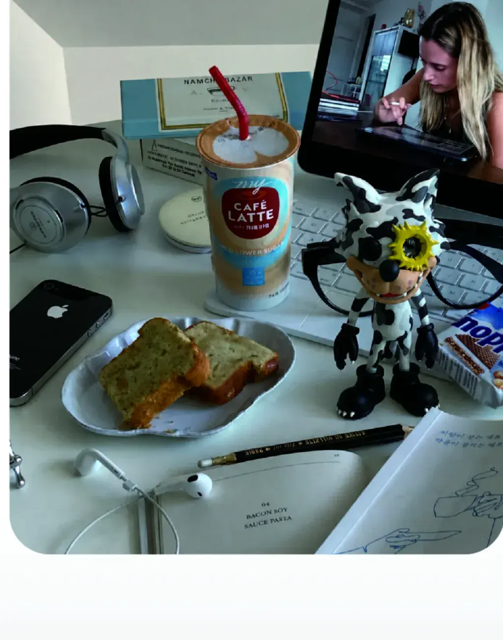 A real white-and-black hard-shell WOWNNY collectible on a creative desk beside a video call, sketchbook, and headphones
